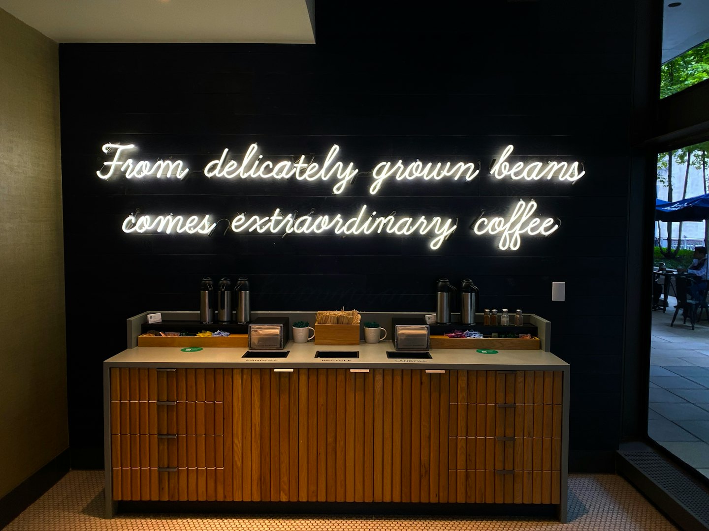 Modern kaffestation med självbetjäning, förnödenheter och sopkärl.
